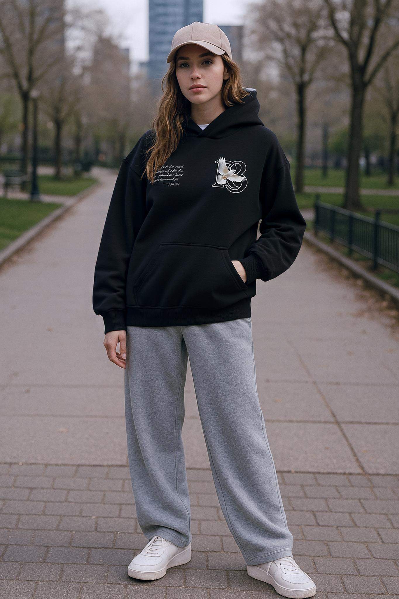 Woman wearing black oversized R3 The Messiah John 3:16 premium cotton hoodie with gray sweatpants and beige cap outdoors