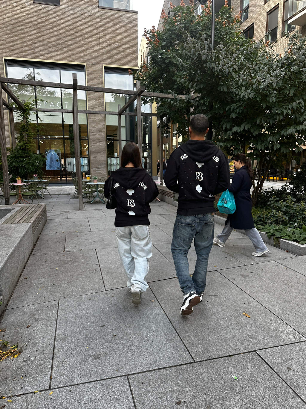 Two people wearing black Clover Nights Zip Hoodies walking outdoors in an urban setting