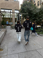 Two people wearing black Clover Nights Zip Hoodies walking outdoors in an urban setting