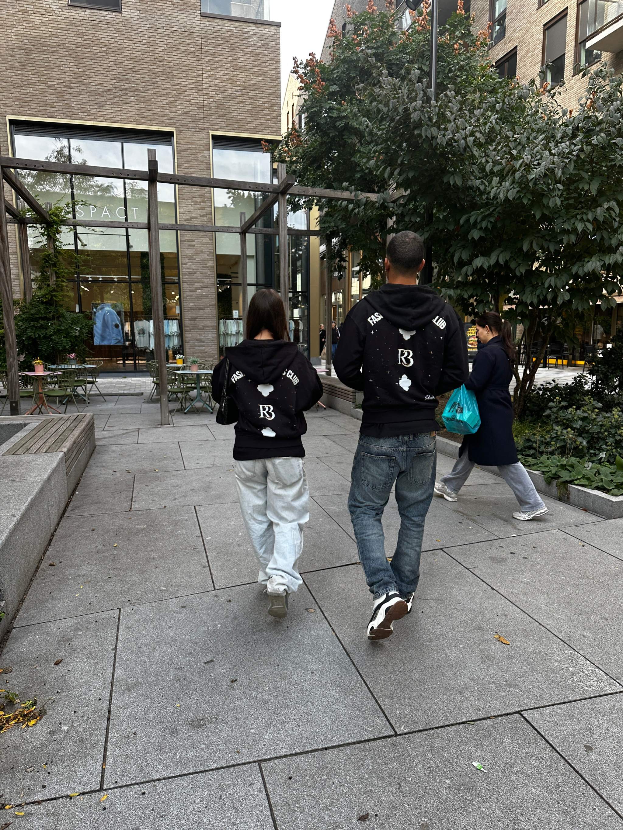Two people wearing black Clover Nights Zip Hoodies walking outdoors in an urban setting