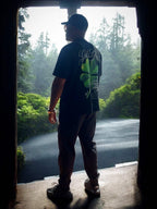 Man wearing black God's Grace Oversized Shirt with clover design standing outdoors in nature